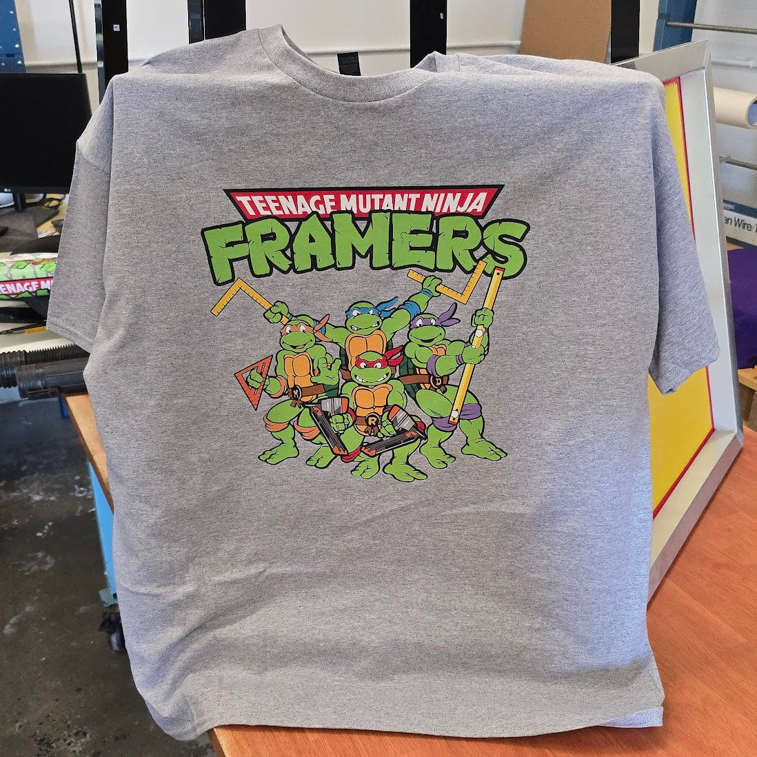 Gray sweatshirt with Teenage Mutant Ninja Framers graphic on a wooden surface.